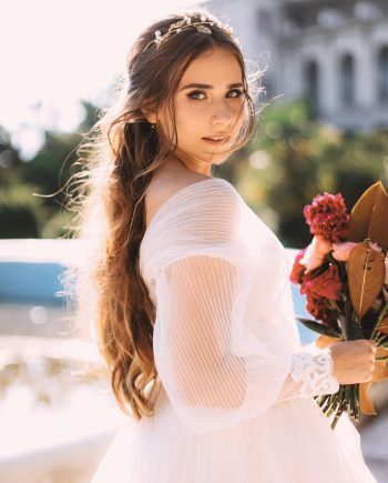 A beautiful bride in a white gown holding a bouquet outdoors. Sunlit and serene, perfect for wedding themes.