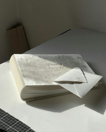 A guestbook with an envelope placed on a sunlit table; minimalist and elegant.