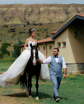 Bride on horseback with groom in countryside setting, perfect wedding moment.