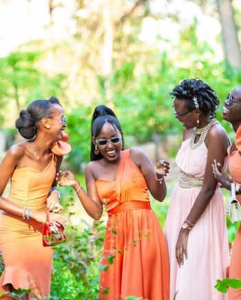Four smiling bridesmaids in vibrant dresses sharing a joyful moment in a lush park setting.