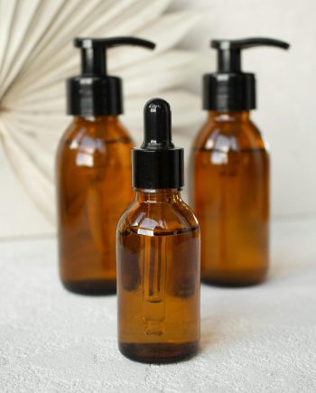 Stylish arrangement of amber glass cosmetic bottles with droppers and pumps on a textured surface.